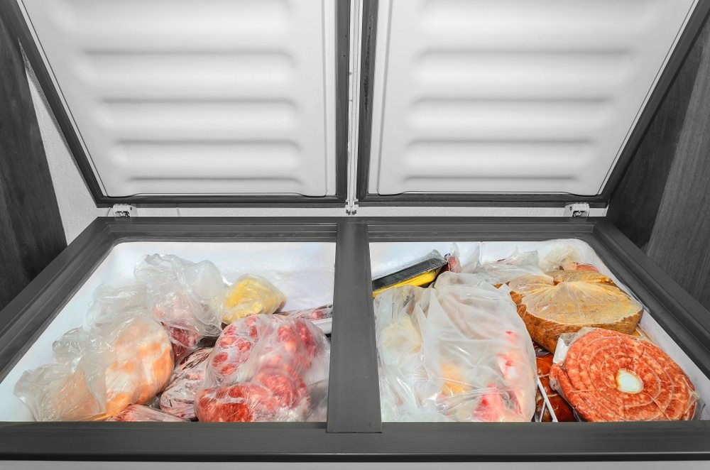 Open chest freezer filled with various frozen foods in plastic bags, illustrating the importance of efficient freezer repair services offered by FixEmApplianceRepair in Oakland.